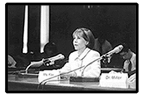 Ms. Fox sits, speaking into the microphone in front of her, at a conference table in a Congressional hearing room.