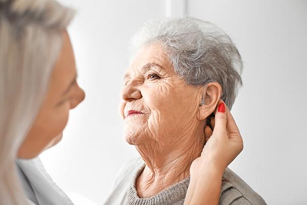 Young female doctor fitting hearing aid on older female's ear.