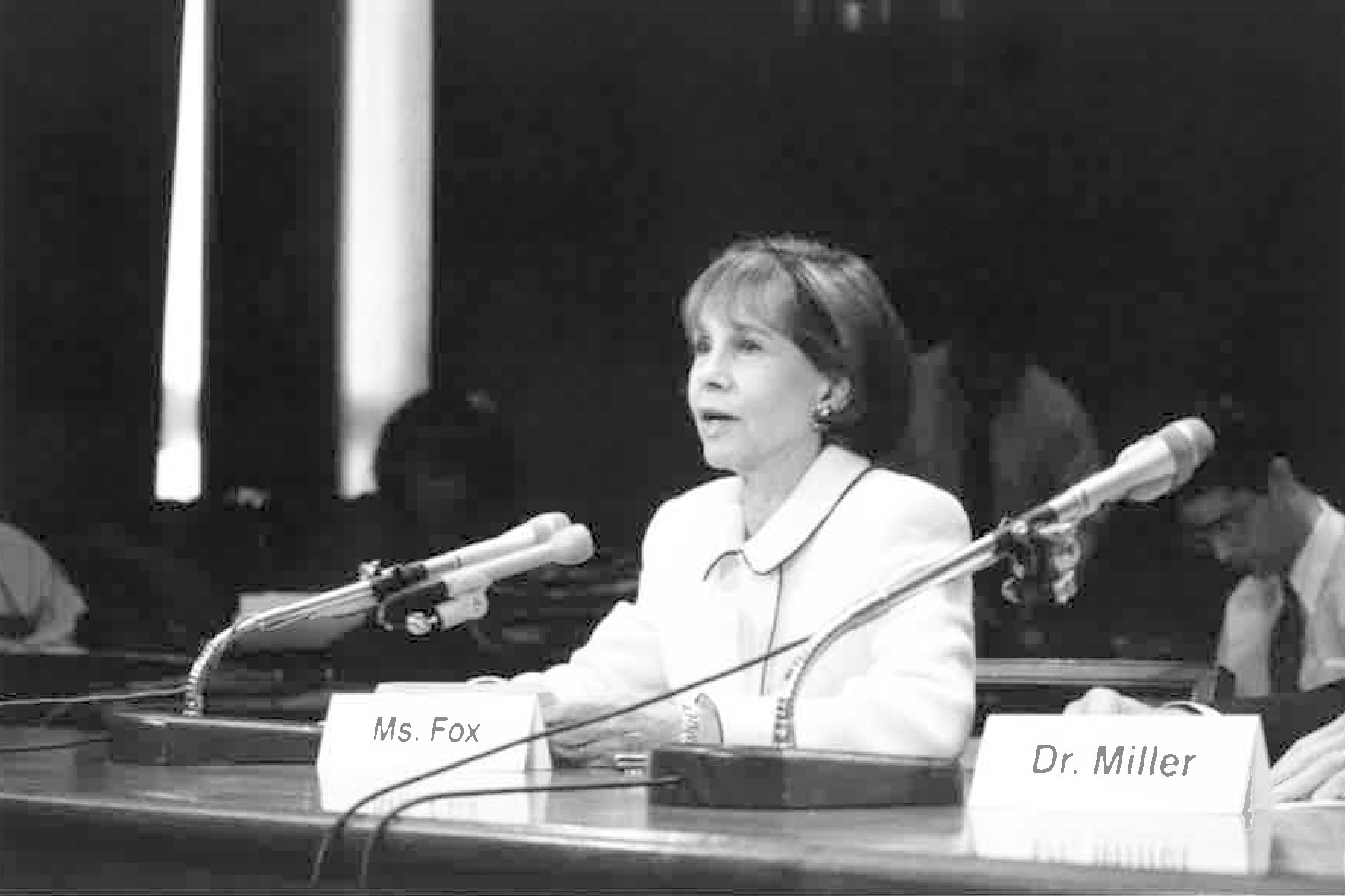 Ms. Fox sits, speaking into the microphone in front of her, at a conference table in a Congressional hearing room.