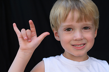 A young boy signs "I love you."