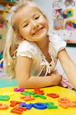 Smiling young girl at low table with colorful, toy block letters