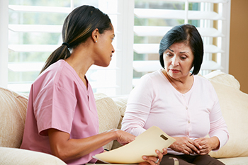 Young woman in pink scrubs holding a clipboard asks survey question to middle-aged woman in her home.