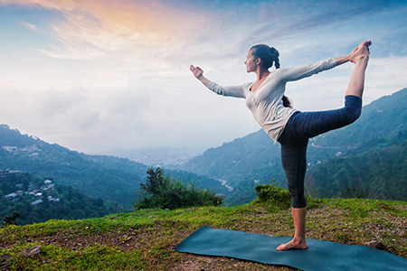 A woman balancing while doing yoga outside.