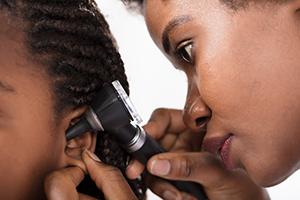 Doctor checking child's ear with otoscope.
