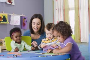 Three toddlers coloring at table with a teacher.