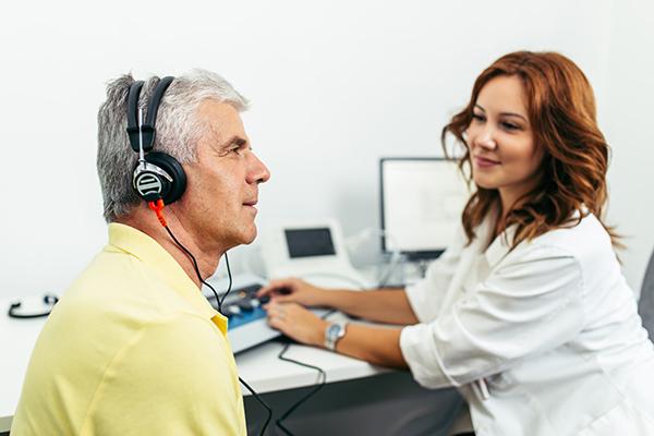 Una audióloga le da una prueba de audición a un hombre mayor en un consultorio del médico.