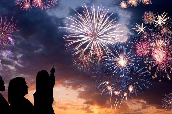 A silhouette of a family with a little girl pointing to large fireworks in the sky.