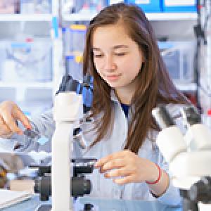 A high school student looking in a microscope. 